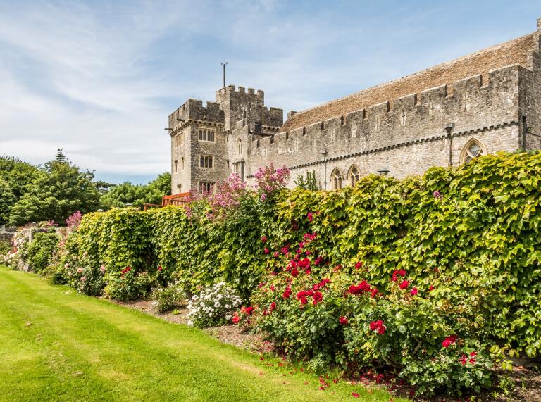 A castle wall next to a flower bush and a green lawn.