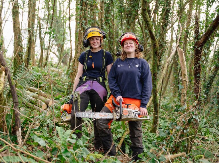 Llys y Fran Rangers wear protective equipment and hold chainsaws in the forest (left to right- Millie and Katie)