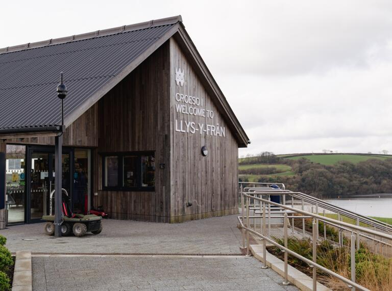 Wooden building by lake with sign Welcome to Llys y Fran