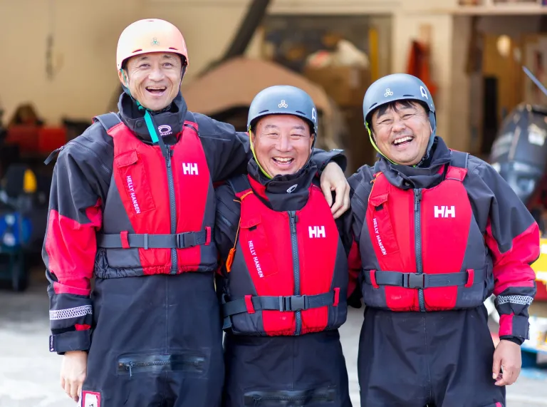Three male Japanese fire brigade members stood next to each other smiling in sea rescue clothing at UWC Atlantic College