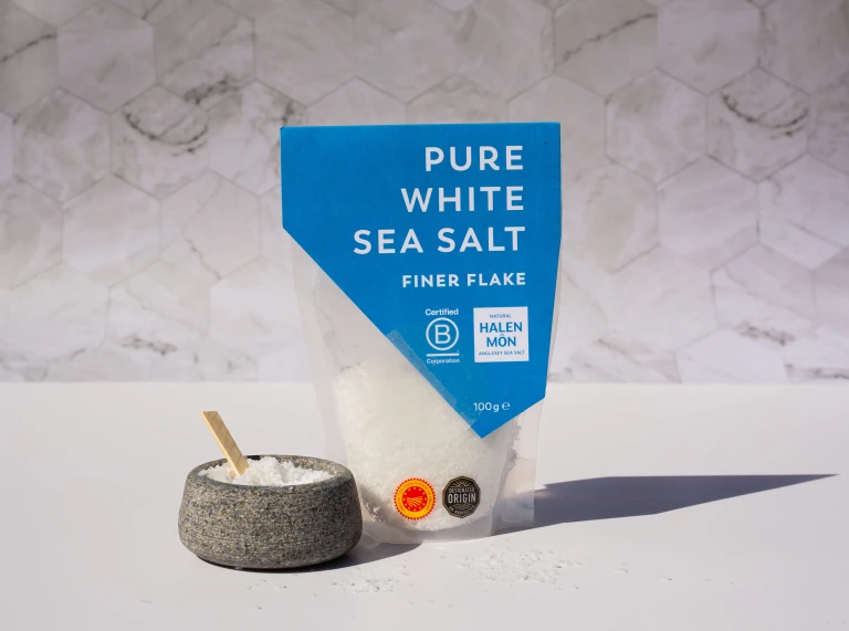 A packet of Halen Mon Pure White Sea Salt Finer Flake from Wales next to a small bowl with some loose salt in it