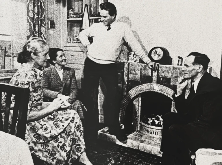 A black and white photo of four adults chatting in a living room, with Richard Burton standing by the fireplace and the others seated.