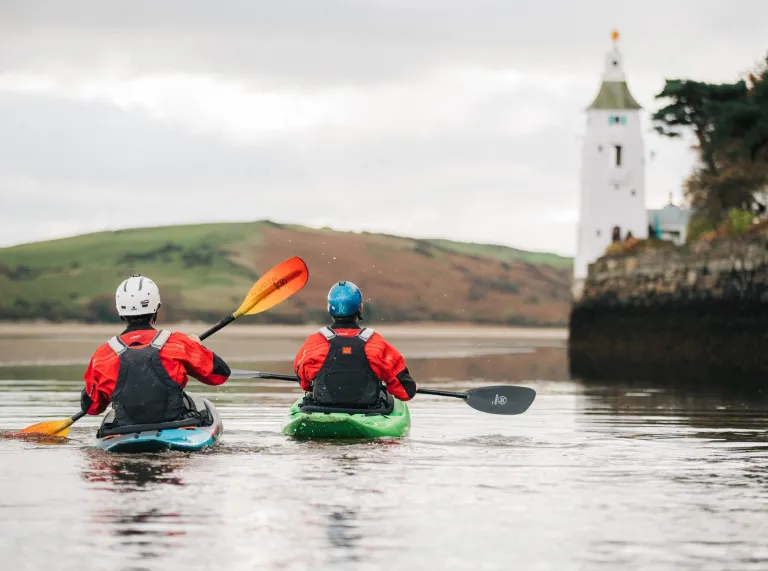 Two people kayaking on the sea with a lighthouse in the background