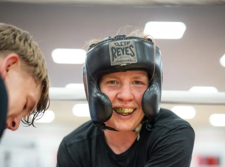 Rosie Eccles smiles during a break in sparring while wearing protective headgear in the boxing ring. 