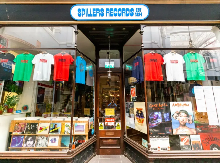 Shopfront of Spillers Records in Cardiff, displaying vinyl records, music posters and colourful T-shirts in its windows. 