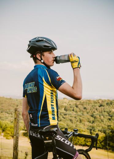 A cyclist is sitting on his bike, resting and drinking from a water bottle