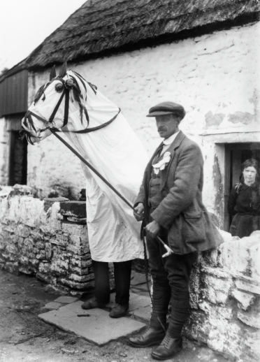 Eine Mari Lwyd und ein Mann vor einem Haus.