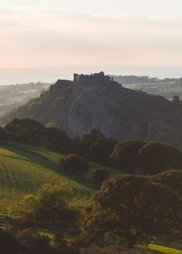 Blick auf Carreg Cennen Castle, eine Burg, die inmitten grüner Hügellandschaften auf einem Felsen thront.