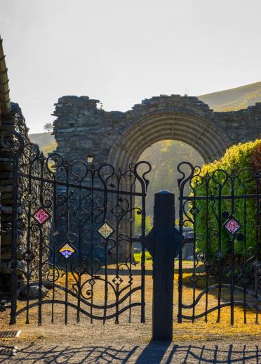 Blick durch ein schwarzes Gitter-Tor vor der Ruine einer alten Abtei. 