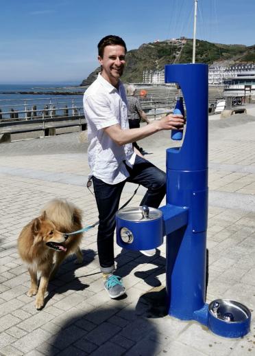 Ein Mann mit Hund füllt seine Wasserflasche an der Nachfüllstation in Aberystwyth auf.
