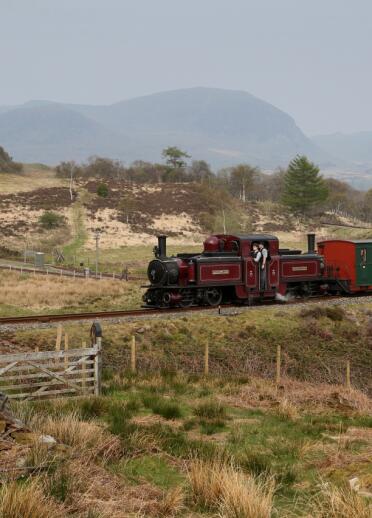 A red and green steam engine moving along a track in front of a mountainous backdrop