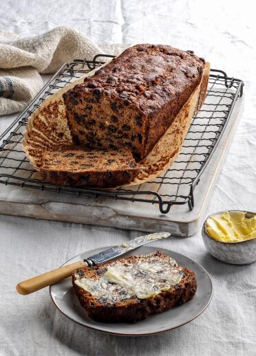 A loaf of bara brith and a slice with butter on it.
