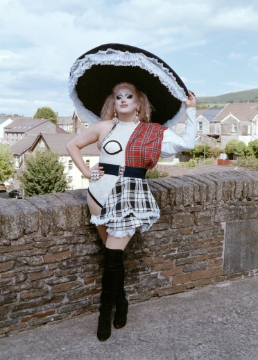 Drag queen Catrin Feelings vestida con un atuendo moderno de dama galesa, de pie sobre un viejo puente de piedra