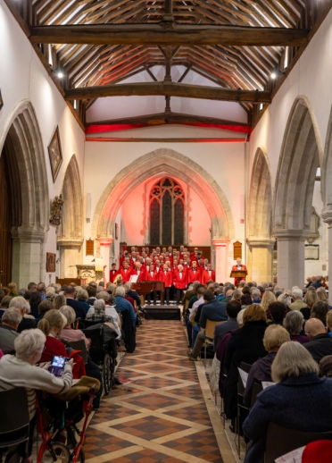 Choir in red jackets performing at the front of a church to a seated audience.