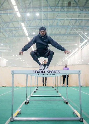 Jeremiah Azu jumping over hurdles during an indoor athletics training session.