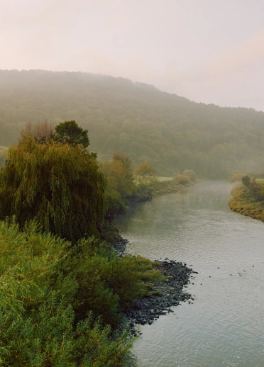 White building on the river bank with hills in the background