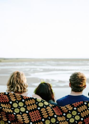 vue de dos de cinq personnes enveloppées dans une couverture colorée avec la mer en arrière-plan.