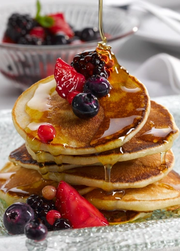 Une pile de crêpes avec des fruits et du sirop.