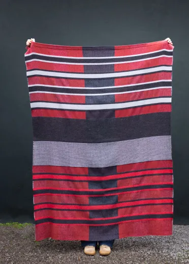Una persona sostiene una manta de rayas rojas, blancas y azules, tejida a mano por la artista textil galesa Llío James.