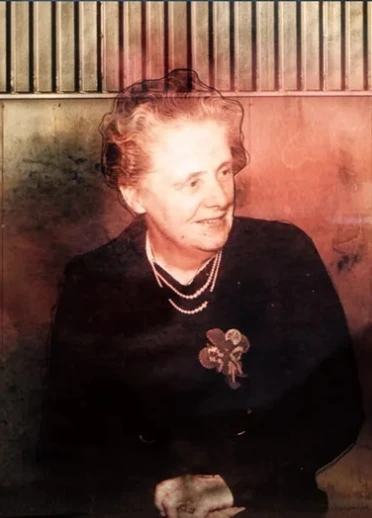 Sepia toned hologram image of Elizabeth wearing a pearl necklace with a flower brooch on against a dark top