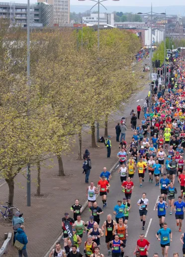 A large group of people running the marathon through a tree lined street