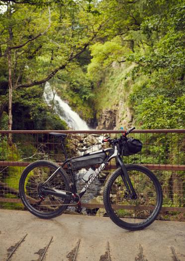 A mountain bike leaning on a fence in front of a waterfall