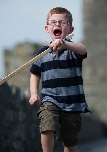 Photo of boy who in focus running with play sword through Harlech Castle which is blurred in the background