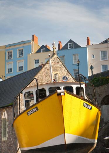Gelbes Boot im Hafen von Tenby bei Ebbe, bunte Häuser im Hintergrund