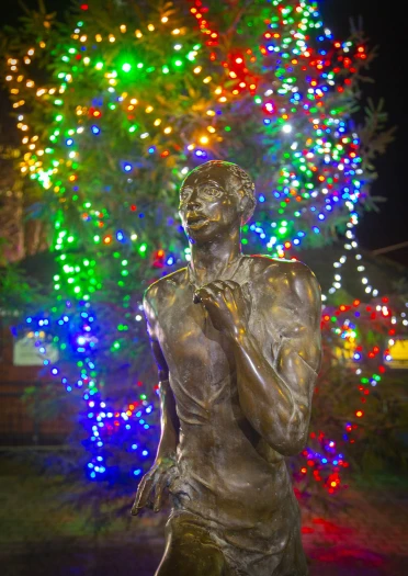 estatua de un hombre corriendo (Guto Nyth Brân) con cadenas de luces multicolores en el fondo.