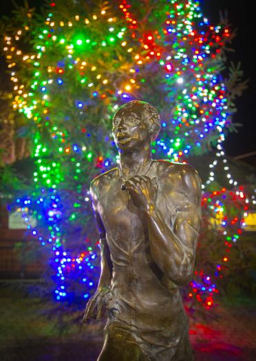 statue of man running (Guto Nyth Brân) with multi coloured strings of lights in background.