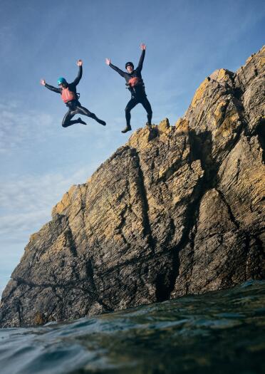 Deux personnes équipées de matériel de sécurité sautent d'un rocher dans la mer.