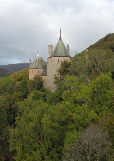 An old, red-brick fairytale castle nestled amidst green trees on the side of a steep hill