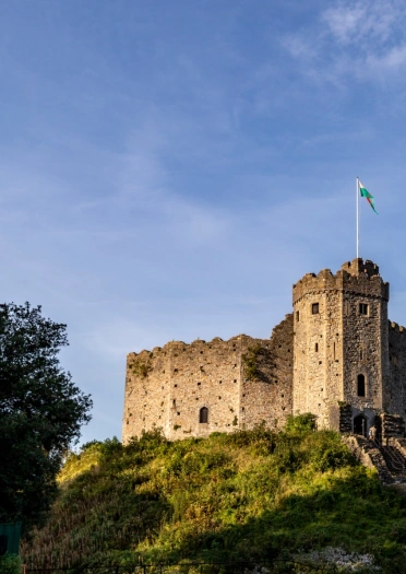 Un castillo fuerte sobre un montículo cubierto de hierba, con una bandera galesa ondeando en la cima.