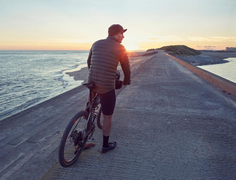 Ein Mann auf einem Fahrrad in Barmouth bei Sonnenuntergang.