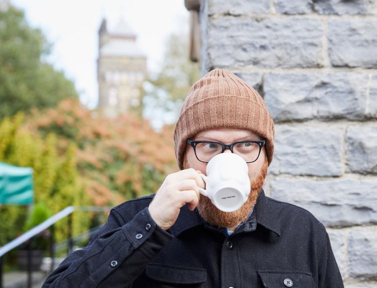 Huw Stephens bebiendo café de una taza blanca en los terrenos del castillo de Cardiff