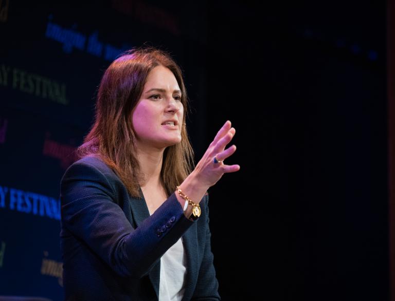 A woman gesticulating with her hand as she presents a speech.