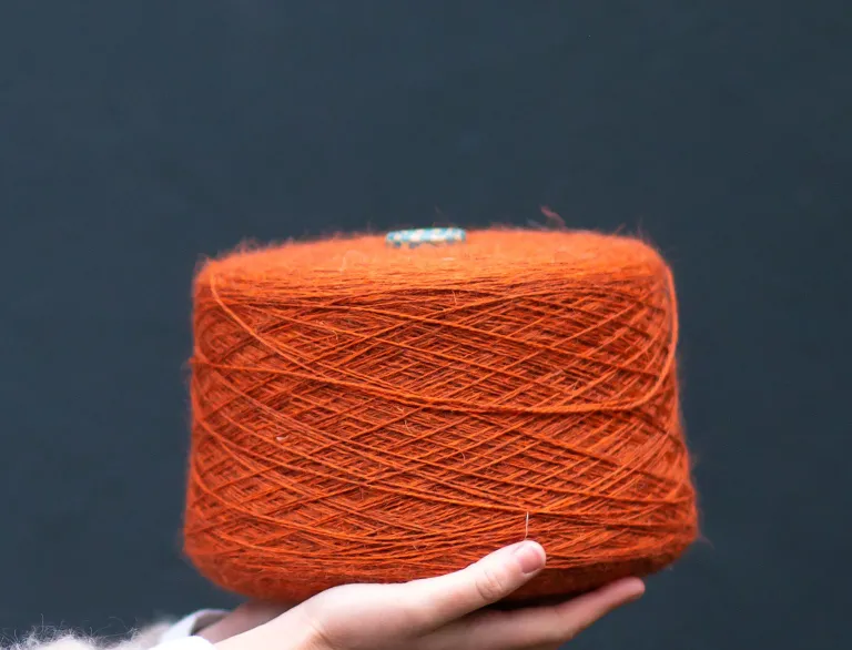 Una mano sostiene un gran carrete de lana de color naranja.