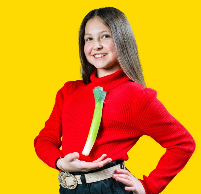 Young girl in a Welsh hat and red jumper standing showing off a leek pinned to her jumper