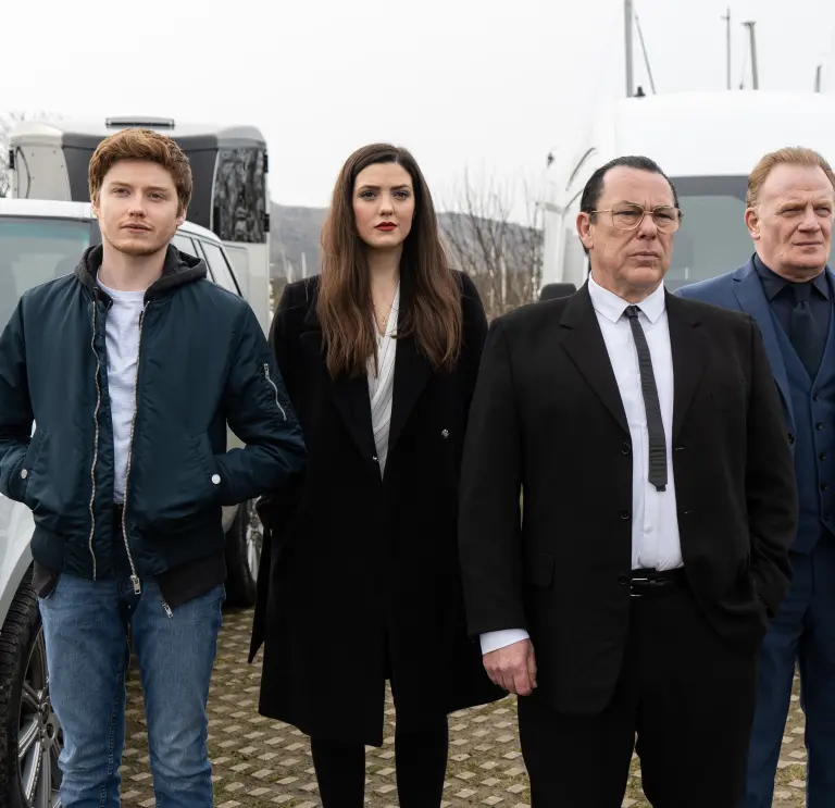 A group of actors standing in front of a car