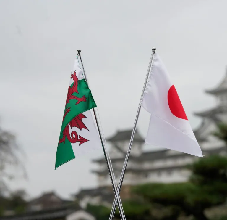 A Welsh flag and a Japanese flag shown in the foreground, with a Japanese castle in the background