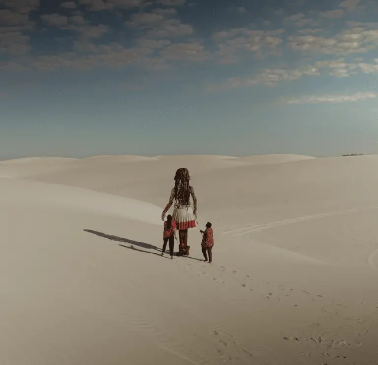Two people walking a giant puppet through the desert