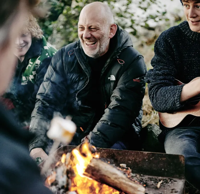 People smiling sitting around a campfire.