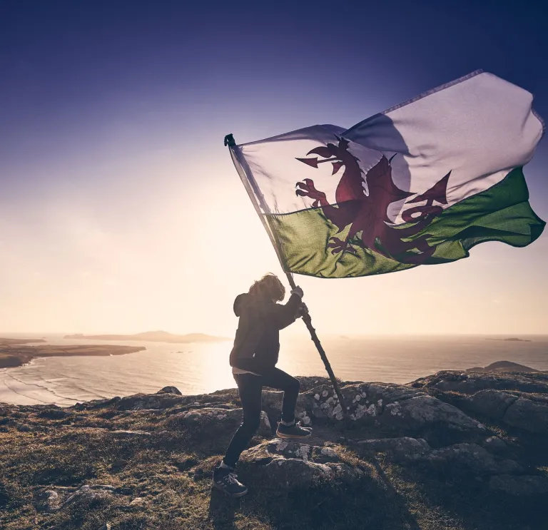 A person on a windy mountain holding a large Welsh flag