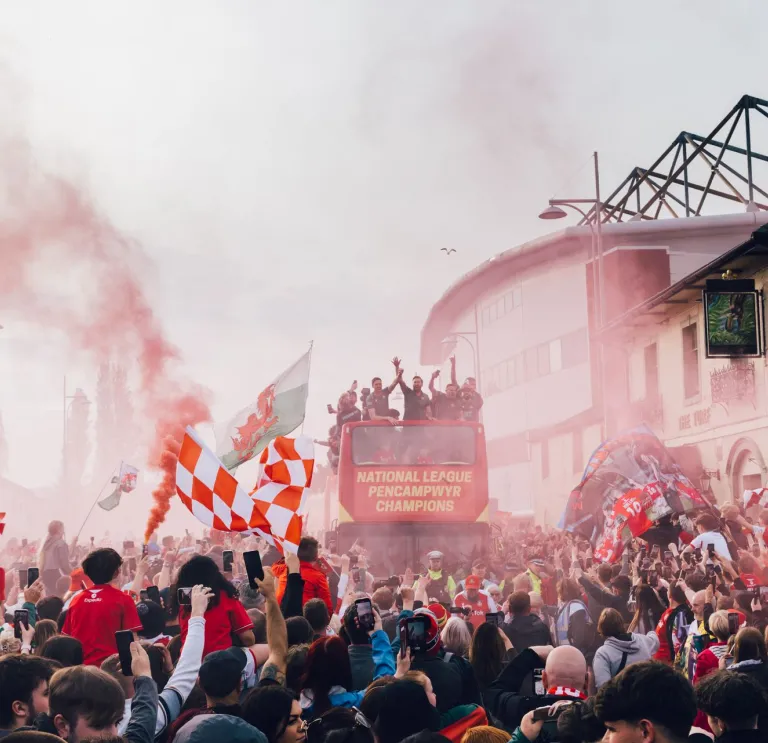 Wrexham football players on a coach travelling past a crowd of people.