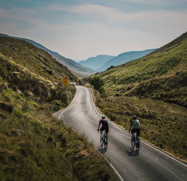 Two people cycling along a mountain road.