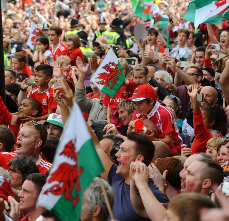A crowd of football supporters holding Welsh flags.