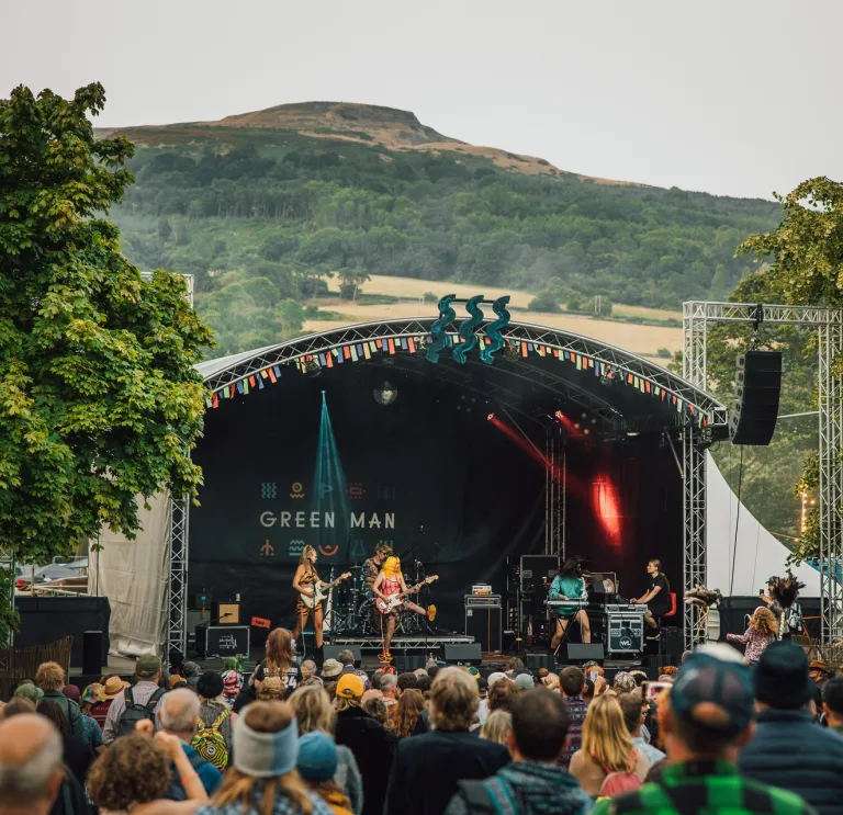 A band performing at the Green Man Festival with a crowd looking on.