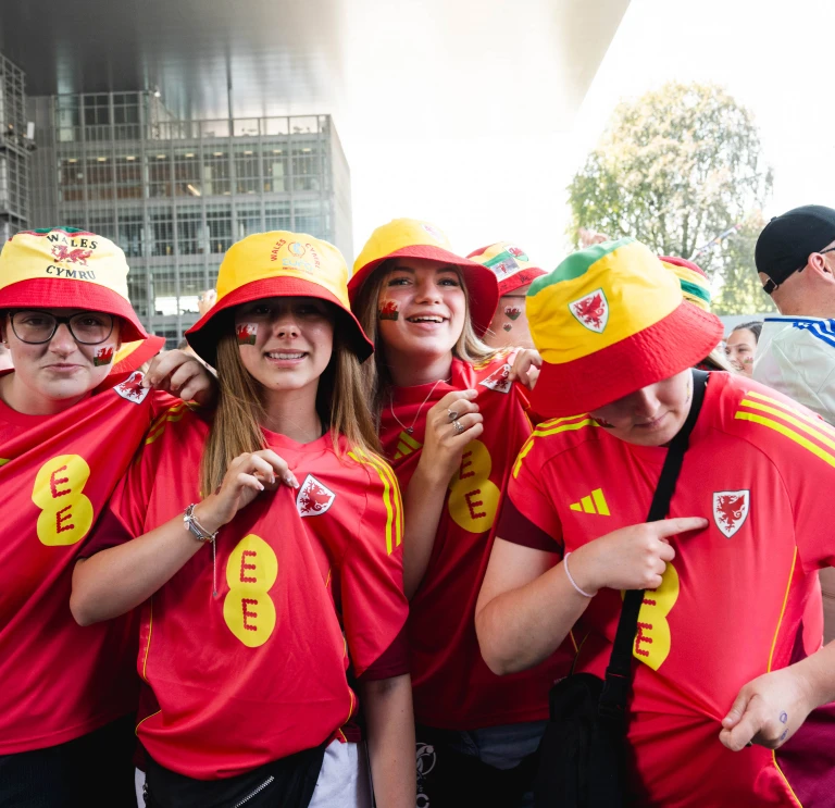 Wales supporters wearing Cymru shirts and bucket hats in a UEFA Women's EURO 2025 fan zone. 