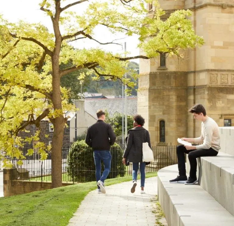 Two people walking and one sat on steps Bangor University 