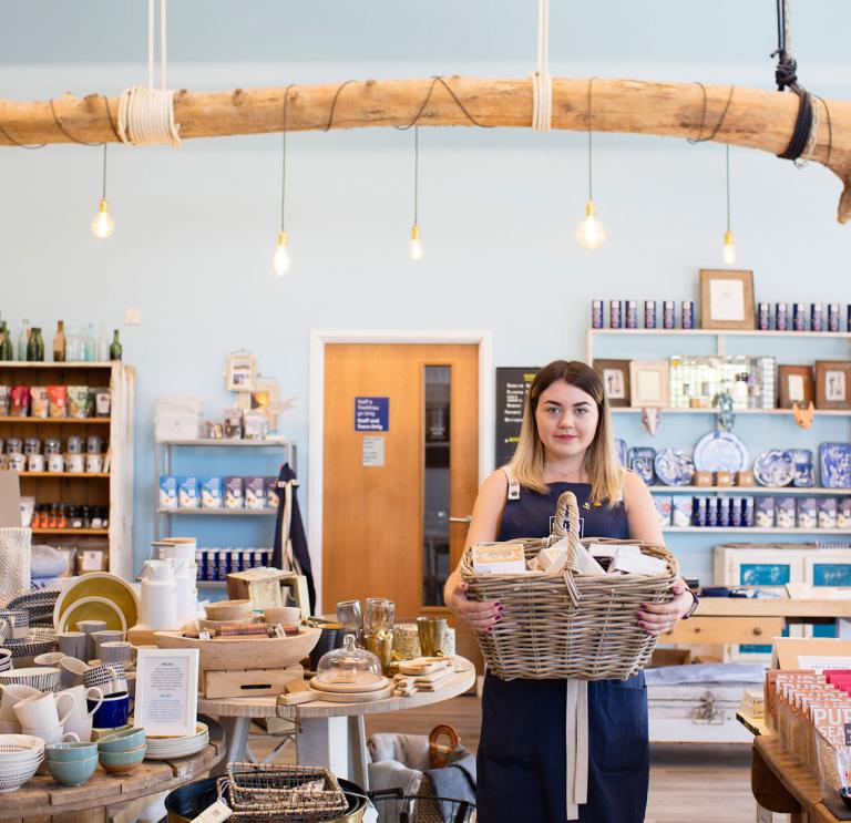 Eine Frau in einem Laden, die einen Korb mit Produkten im Arm hält.